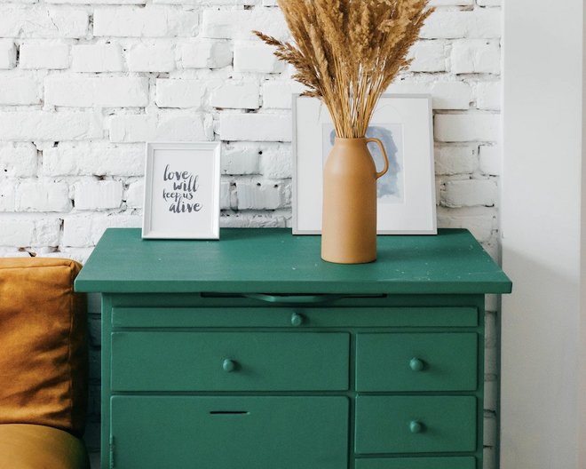 Detail of a chest of green drawers in front of a white brick wall